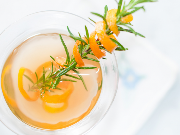 Aerial photograph of a martini with a fresh spring of rosemary as garnish with an orange peel wrapped around it.