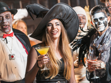 Woman dressed as a witch for Halloween holing a yellow martini in front of other poeple dressed up